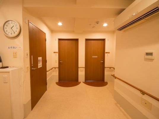 居室前の廊下には、両サイドに手すりが設置されている。男女兼用トイレのドアは木目調である。トイレマークはわかりやすいように大きく表示している。