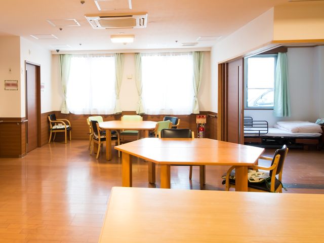 居室とダイニングエリア 共有スペース 広々としたダイニングエリアには木の温もりを感じるテーブルと椅子が配置され、快適な食事や語らいの時間を過ごせる環境が整っています。窓際の明るい光が室内に優しく差し込み、ひと息つくのに最適な空間です。