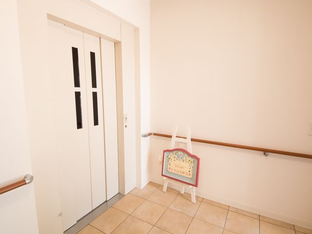 清潔なエレベーター入口 エレベーター 手すり沿いに優しい色合いの壁が、ご高齢の方の歩行をサポートします。歓迎の気持ちを込めた看板も設置しております。