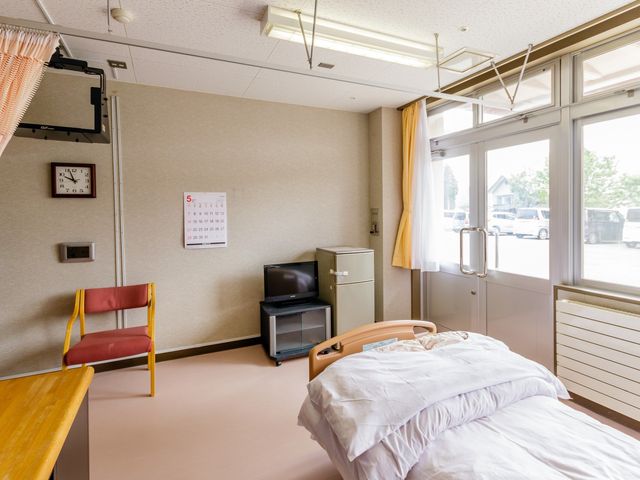 快適な居室 居室 ゆったりとしたベッドと清潔感のある窓際の椅子が配置された居室です。明るい日差しが心地よい空間で、安心して過ごせます。