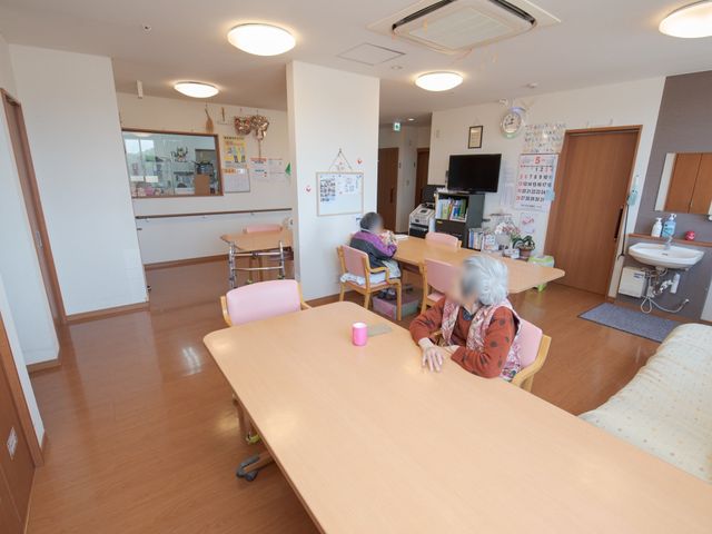 居室内のゆったり空間 食堂 明るく開放的な居室で、利用者の方がくつろいでいる様子が映っています。日当たりも良く、心地よい時間を過ごせる設計になっております。