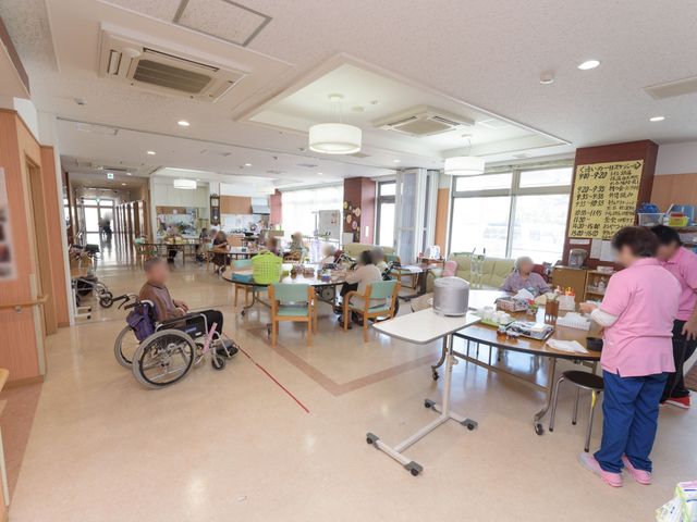 広々とした明るい食堂 リビングダイニング 広々とした食堂では、利用者が食事や様々な活動を楽しんでいます。スタッフが手厚いサポートを提供している様子が伺えます。