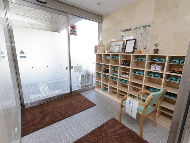 入口エリアと靴箱 エントランス 明るく清潔感のある入口には多くの靴が収納され、訪れる方々を温かく迎えています。靴箱の横にはゆったりとした椅子が置かれ、靴の着脱に便利です。