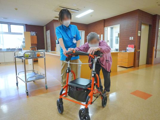 歩行器を使って歩くおばあさんとそれを支える介護職員