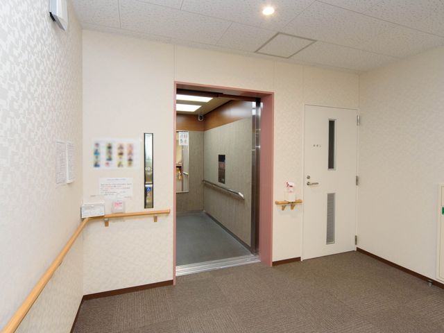 清潔な廊下と掲示物 エレベーター 手すりが設置された落ち着いた色合いの廊下です。壁には情報共有のための掲示物もあります。