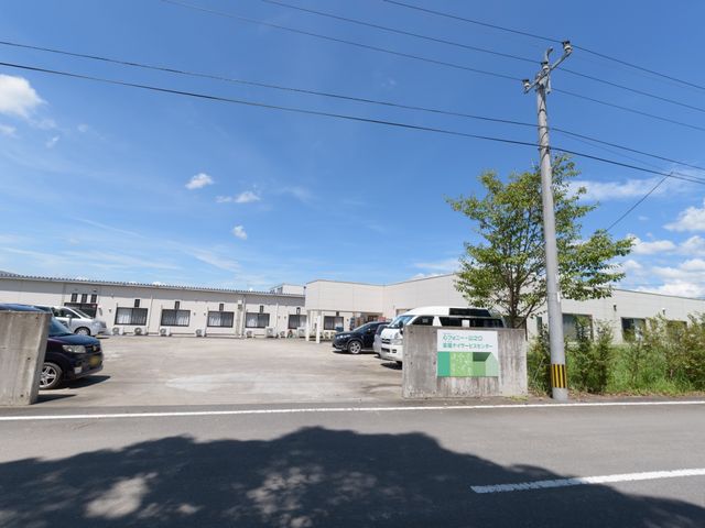 晴天下の施設外観 外観 広々とした駐車場があり、利用者の安心したアクセスを支援します。自然光溢れる環境は、新しい職場としてもご検討いただけます。