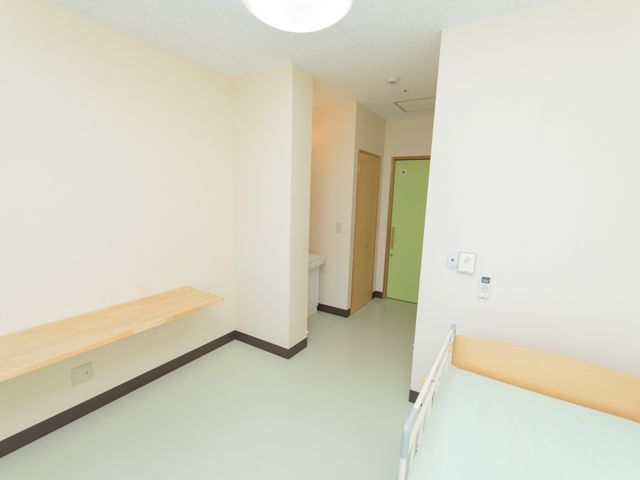 居室の広々とした角度 居室 シンプルで落ち着いた色合いの個室です。木製の棚を備え、ゆったりとした生活空間が確保されています。