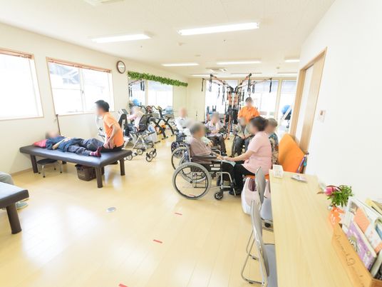 ベッドやトレーニング用のマシンがたくさん並んだ部屋があり、スタッフと入居者様がトレーニングを行っている。
