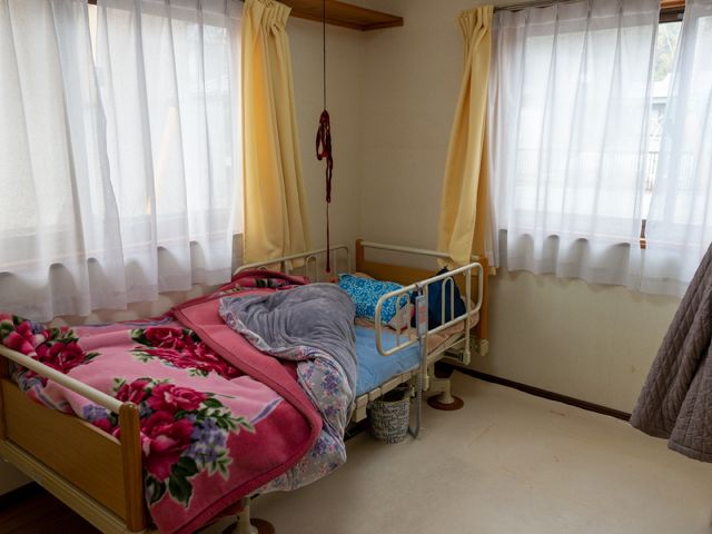 居室のベッドとカーテン 居室 ゆとりの空間を備えた居室で、窓からは自然光が差し込み、明るく温かな雰囲気が演出されています。ベッド周りは清潔感があり、居心地の良さが感じられます。