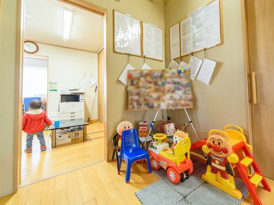 廊下の一角に滑り台に足漕ぎ車、小さな椅子に人形など小さな子供たちが遊べる遊具を設置している。入居者様の写真も沢山飾っている。