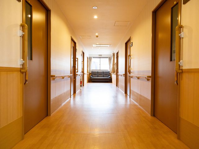 広い廊下の風景 廊下 広々とした廊下は明るく、手すりが設置されているため安心して移動が可能です。奥の窓から自然光が差し込み、温かみのある空間になっています。