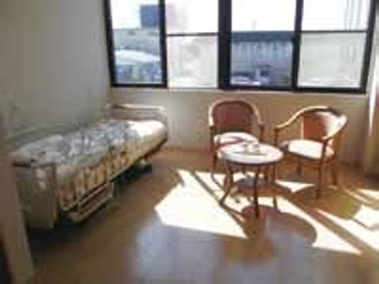 介護用ベッドと椅子、小さなテーブルが並んでいる施設内の居室の様子