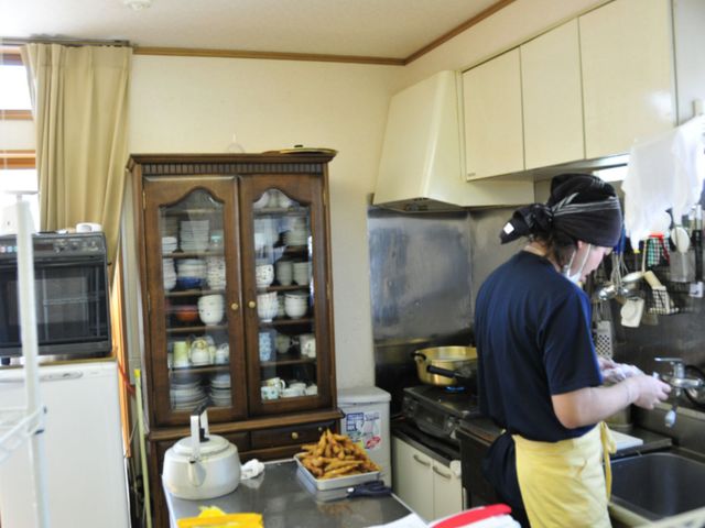 キッチンで作業する人 日常風景 温かみのあるキッチンで調理される手作りの食事が、毎日の楽しみの一つです。献身的に業務に取り組むスタッフがいる環境です。