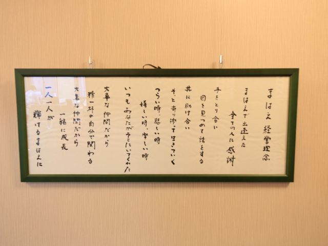 掲示物の書かれた和歌 経営理念 美しい書の和歌が飾られた壁は、日々の暮らしに落ち着きと和の心をもたらします。美しい文字を眺めながら、心穏やかなひとときを過ごせる空間です。