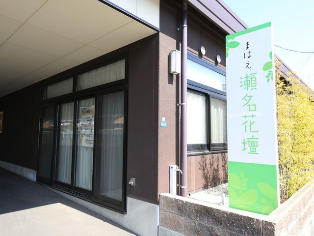 施設のエントランス看板 外観 落ち着いた色合いの入口横に、緑の葉をあしらった看板が立てられております。周りの自然と調和し、訪れる方を温かく迎えてくれる雰囲気です。