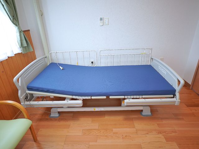 居室の介護用ベッド ベッド 高さ調節が可能な機能的な介護用ベッドです。周りは清潔感のある床と壁で明るい印象を与えます。