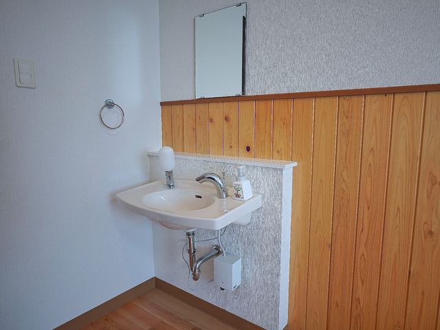 洗面所の壁と手洗い器 洗面台 手洗い後の清潔を保つために、壁に取り付けられたハンドソープとミラーが設置されています。清潔感のある木目調の仕上げが心地よい空間を演出しています。
