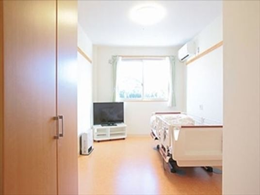 施設の写真 テレビと介護用ベッドが置いてある施設内の居室の様子。窓から日差しが差し込んでいる