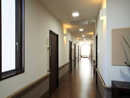 まっすぐに続く廊下と手摺が付いている壁。両側に個室が並んでいる