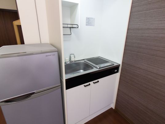 居室の一角に、簡易キッチンが設置されている。IH調理器が一口ついている。左横には冷蔵庫が置かれている。