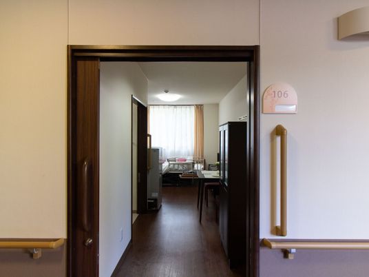 居室の入口は、大きな取っ手がついた木製の引き戸である。入口の横に居室番号が表示されていて、その下に縦方向の大きな手すりがある。