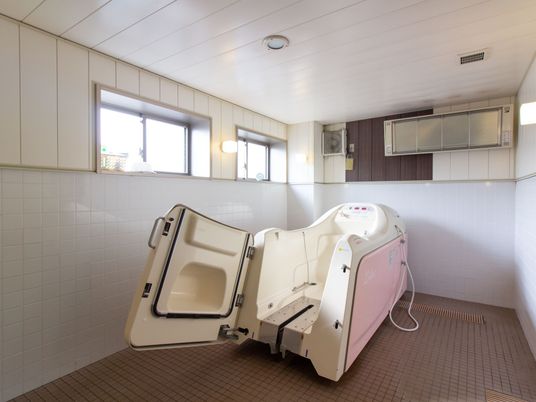スライドして浴槽に入ることができる介護浴槽がある。浴室の壁には、換気扇とパネルヒーターが設置されている。