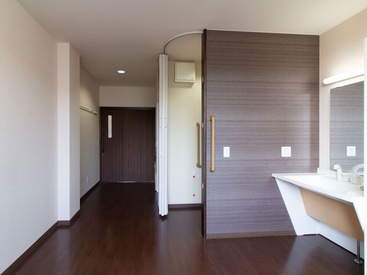 居室に大きな鏡や照明がついた洗面台が設置されている。じゃばらカーテンで仕切ることができるスペースにトイレがある。