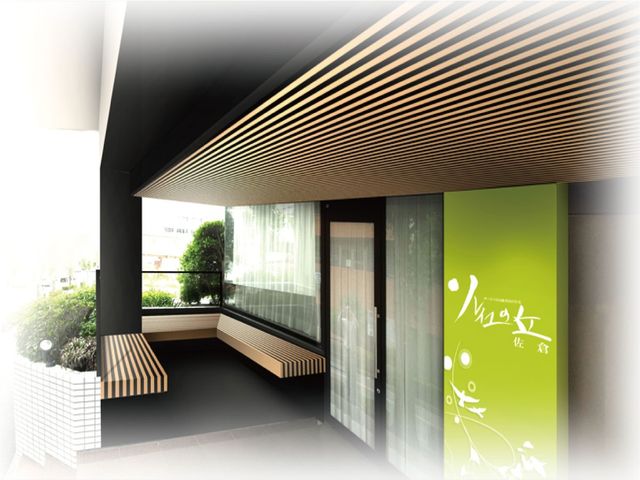 緑の看板がある玄関 エントランス   木目の天井とベンチが印象的な落ち着いた玄関です。外の植栽が見え、明るさも感じられます。
