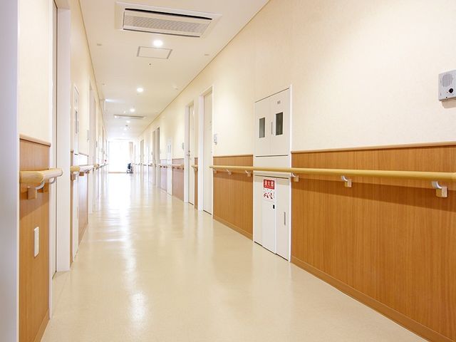 手すり付き綺麗な廊下 廊下 壁に手すりが備えられた清潔感のあふれる廊下です。遠くには車いすを使用されている方が見え、スムーズな移動が考慮されています。