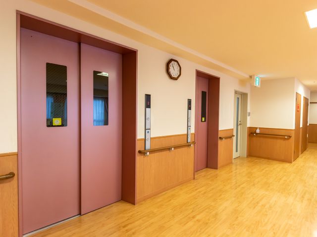 清潔な廊下の様子 エレベーター ゆったりとした廊下はバリアフリー設計で、移動が安全かつスムーズです。周囲は明るく、時間を確認しやすい掛け時計も設置されています。