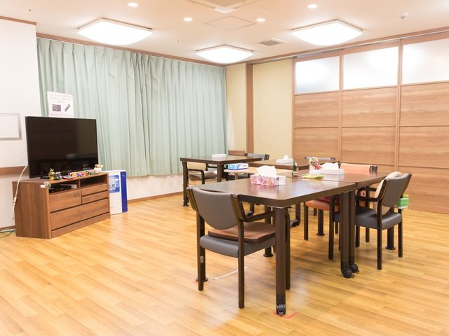 共用リビングの様子 食堂 広々としたリビングは木目調のインテリアが温かみを感じさせ、テレビやテーブルが配置されています。利用者の皆様が共に時間を過ごす憩いの場となっております。