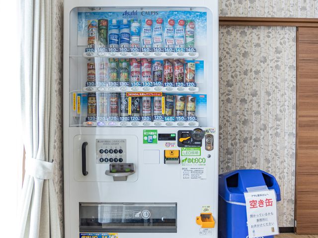 ドリンク自販機と分別ごみ箱のある休憩室 休憩室   飲み物の自販機と空き缶用のごみ箱が置かれた休憩しやすい空間です。明るい窓辺で、スタッフの合間のひと息にも使いやすそうです。