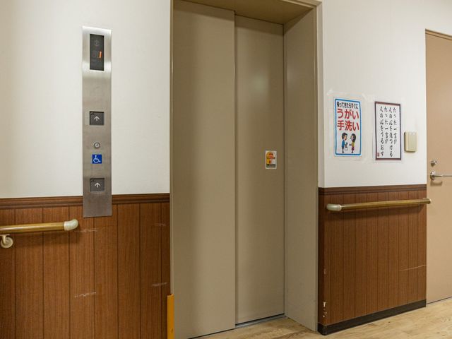 エレベーター前の廊下 廊下   木目調で落ち着いた雰囲気の廊下です。手すりやエレベーターがあり、移動しやすい工夫が見られます。