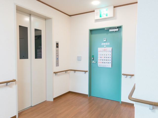 清潔な廊下のエレベーター エレベーターホール 手すりが整っており、計画的なカレンダーが配置された廊下です。スタッフや入居者が安全に移動できる環境が整っています。