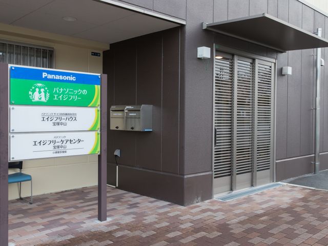 エントランス看板と椅子 玄関 きちんと掲示された看板が訪問者を迎え、休憩できる椅子も用意されています。清潔で整った入口は訪れる方に安心感を与えます。