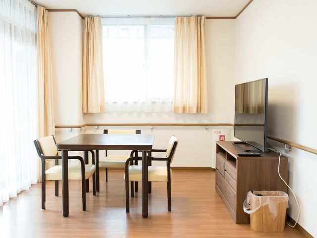 居室のテーブルとテレビ 食堂 ゆったりとした空間で日々のくつろぎを。テーブルと椅子が配置された明るい居室は、快適な生活空間を提供しています。
