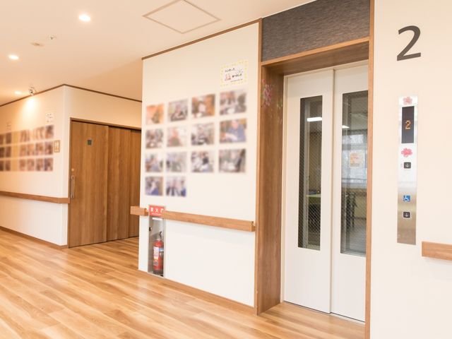 清潔な廊下の一角 エレベーターホール 床が木目調であたたかみのある廊下が広がっており、落ち着いた雰囲気の中でお仕事ができます。壁には楽しげな掲示物があり、明るい印象を与えています。