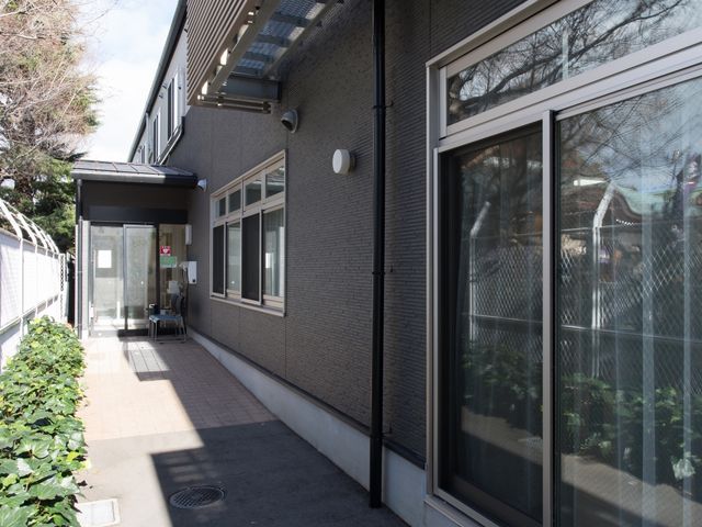 清潔な建物のエントランス 通路 木々に囲まれたエントランスは、清潔感があり、安心してお仕事が始められる雰囲気です。明るさと開放感を感じさせるガラス張りの扉が印象的です。