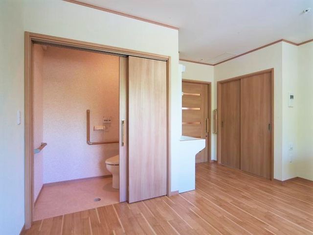 バリアフリーの洗面台付トイレ 居室 使いやすさを考えた洗面台付トイレが設けられており、安心して生活できる環境が整っています。木目調の床が温もりを感じさせ、ゆったりとした時間を過ごせそうです。