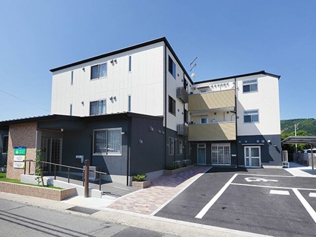 施設の外観 外観   白と濃い色の外壁が印象的な建物です。駐車スペースや段差の少ない出入口が見え、出入りしやすそうです。