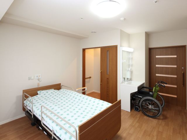 明るい個室のベッドと車椅子 居室 ゆとりを持った清潔な個室には、必要な家具が整っており、快適な毎日を過ごすことができます。安心のバリアフリー設計で車椅子の方もスムーズに動けます。
