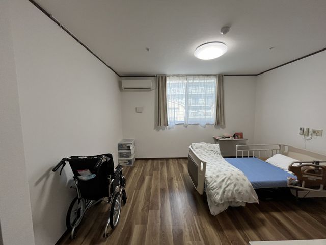 ベッドと車椅子の居室 居室 木目調の温かみある床が特徴の居室です。窓から自然光が入り、明るさも感じられます。