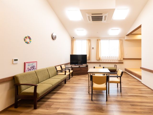 落ち着いた雰囲気の共用スペース 談話室 暖かみのある木目調のリビングです。ソファやテーブルが配置され、ゆったりと過ごせる空間が整えられています。