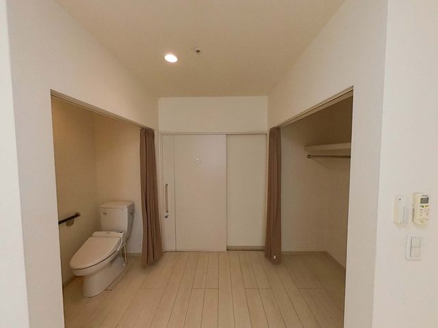 収納スペースとトイレ トイレ 木目調の床にクラシックなトイレと広い収納スペースが設けられています。控えめな照明が優しい雰囲気を作っています。