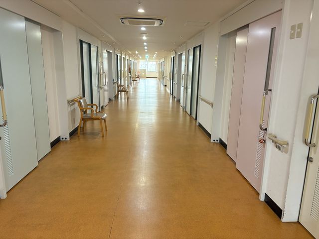 明るい廊下 廊下   両側に居室の扉が並ぶ、まっすぐで見通しのよい廊下です。手すりと椅子があり、移動しやすい環境が整っています。