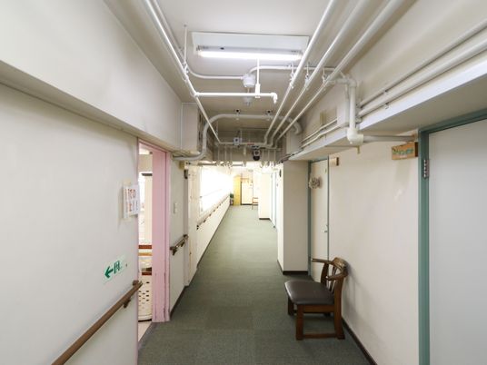 手すりが取り付けられれている廊下で、途中にベンチが置かれている。各居室横には、木製の表札が掛けられている。