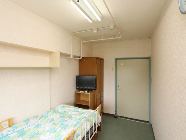 居室の一角とベッド 居室 配置が整然とした居室の一部です。必要な備品が備え付けられ、落ち着いた色合いでまとめられた空間が特長です。