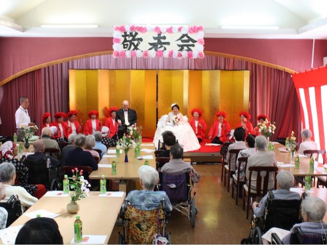 多目的室でのイベント 明るく広々とした多目的室で、色とりどりの衣装を着た方々が楽しそうにイベントを実施している様子です。利用者の方々も笑顔で見守っています。