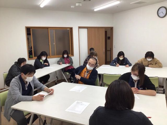研修中の職員が集まる多目的室 多目的室   机を囲んで職員の方々が着席し、資料を見ながら研修を受けています。明るい室内で、落ち着いて学びやすい雰囲気です。