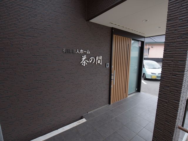 施設入口と看板 外観 落ち着いた色合いのエントランスは、来訪者を温かく迎え入れます。木目調のアクセントが安らぎの空間を演出しています。